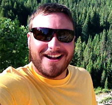 Headshot of Jeremy with sunglasses and evergreen trees in the background