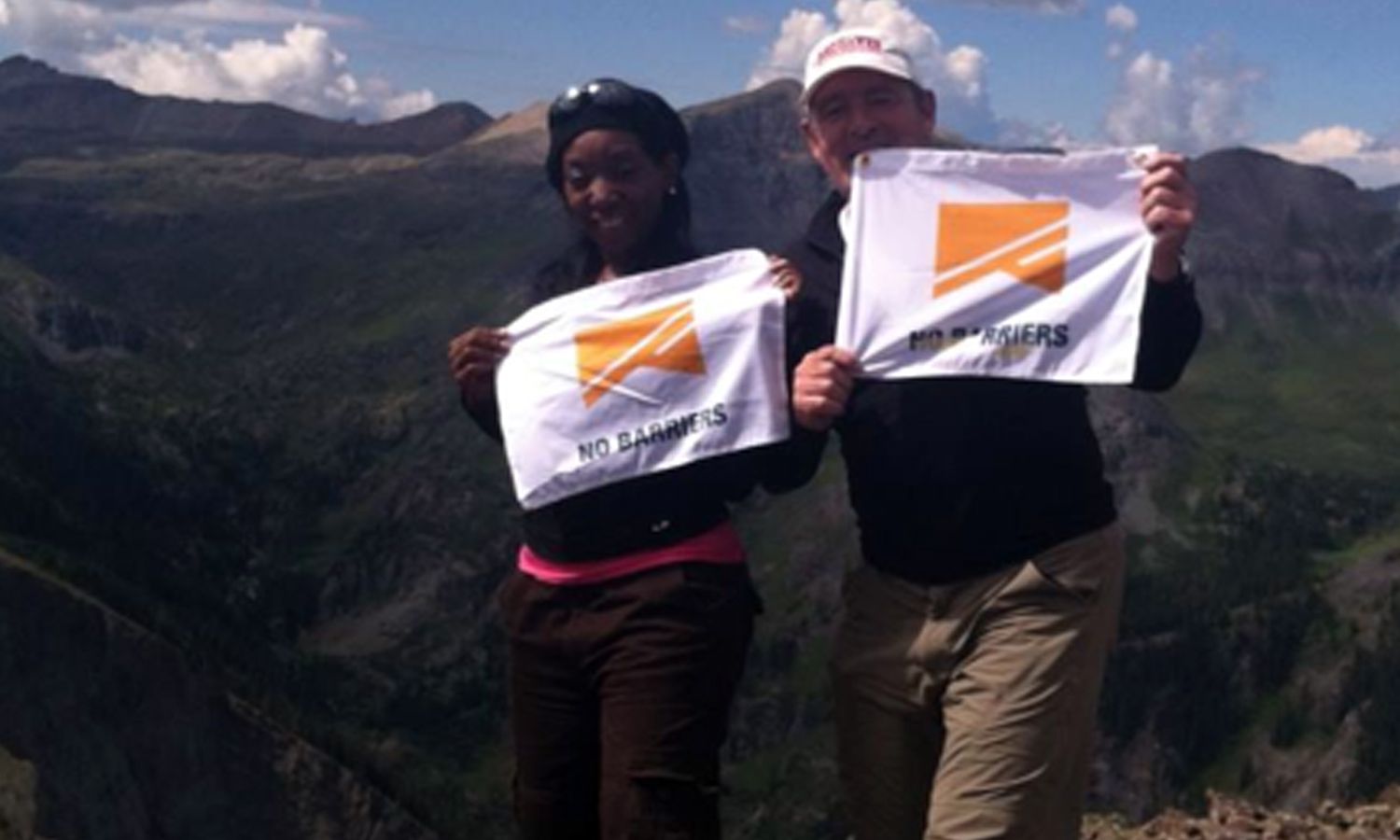 Photo of blog author with teammate at top of mountain. They are holding flags with the logo of No Barriers USA.