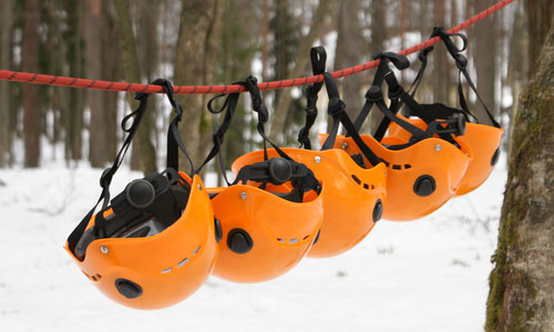 Series of orange climbing helmets hanging on a rope between two trees. Snow is on the ground.