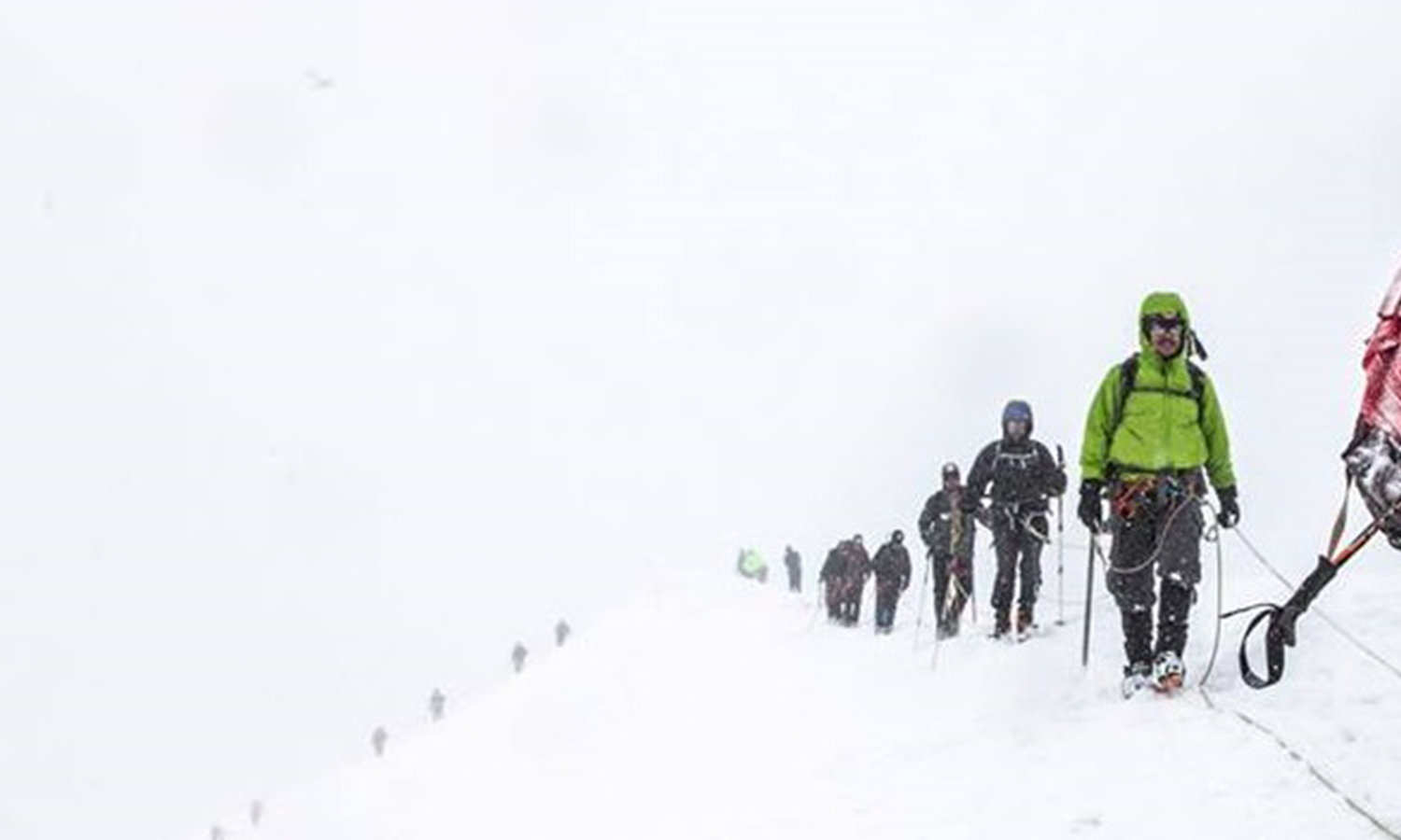 White snowy mountain, all that is visible is a few climbers moving onward toward the camera